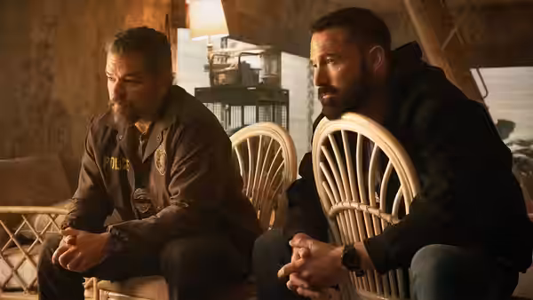 Matt Damon and Ben Affleck seated in wicker chairs inside a room