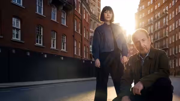 DI Max Arnold (Adrian Scarborough) kneeling beside Astrid Fischer (Anamaria Marinca) on a city street