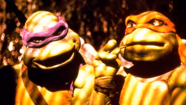 A purple-masked turtle and an orange-masked turtle stand together in the woods