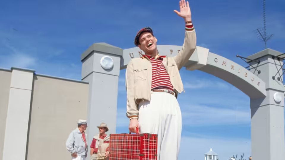 Truman Burbank (Jim Carrey) waving under the Union Omnibus arch with suitcase