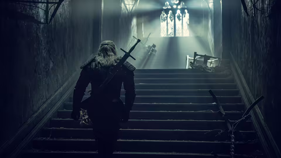 Geralt (Henry Cavill) ascending stone stairs in a dark corridor