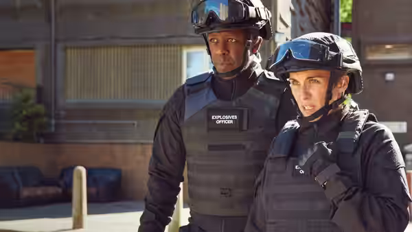 Two explosives officers in tactical vests standing alert outside urban building