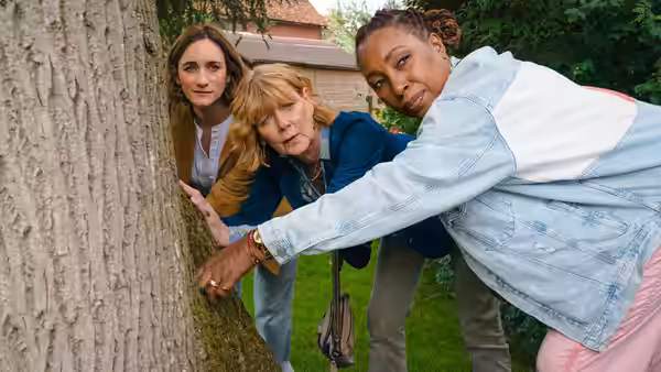 Suzie Harris (Jo Martin) pointing at a tree while two women watch