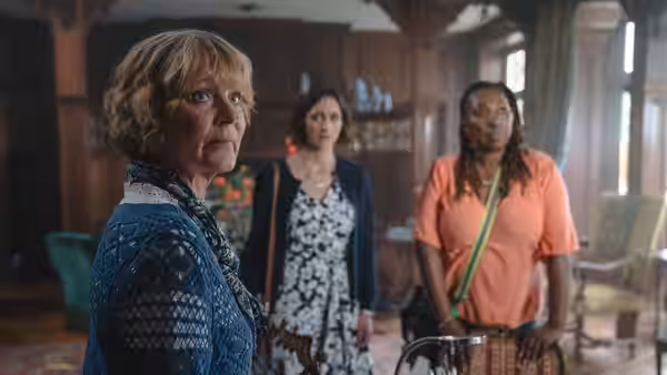 Judith Potts (Samantha Bond) looking ahead with two women standing behind her