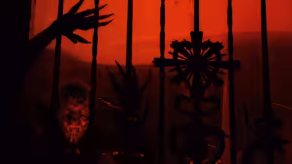 A grotesque demon peers from behind twisted silhouettes against a red-lit backdrop
