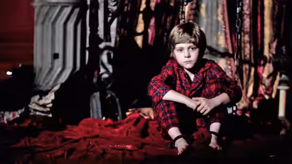 Dalton Lambert (Ty Simpkins) sits on the floor among red fabric and dark furniture