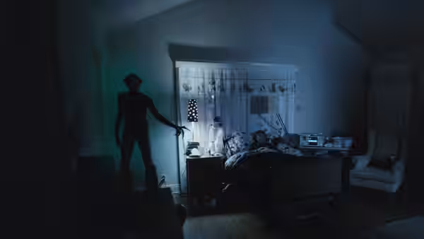 A shadowy figure stands beside a child’s bed in a dimly lit bedroom