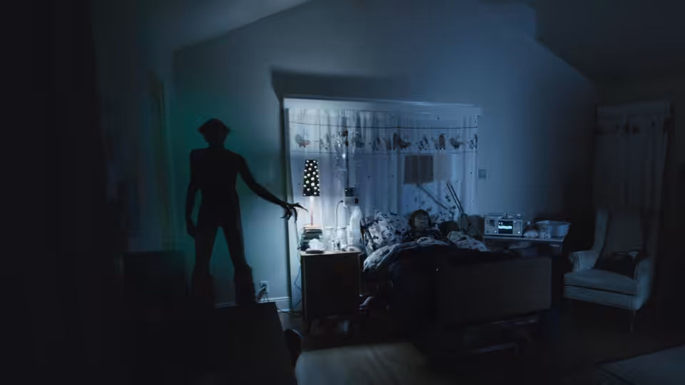 A shadowy figure stands beside a child’s bed in a dimly lit bedroom