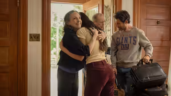 Family group embraces at a doorway as man holds luggage