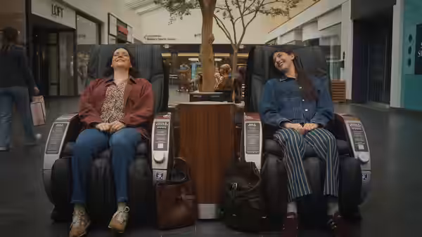 Two young women relax with eyes closed in mall massage chairs