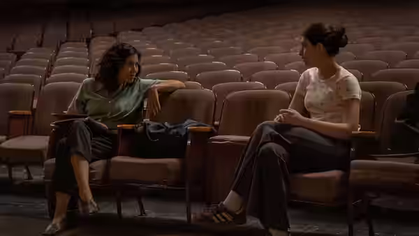 Two women sit talking in rows of empty theater seats