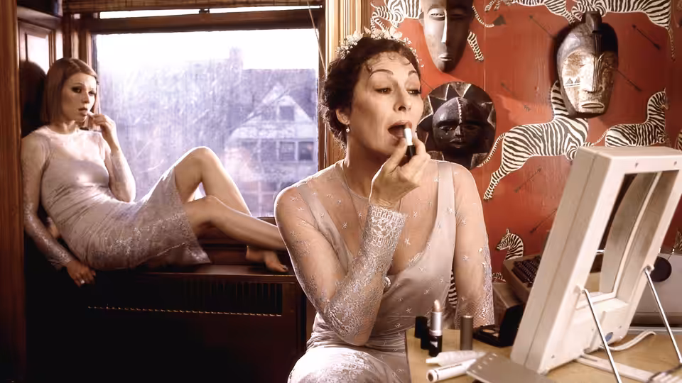 Two women in white dresses apply makeup inside a room with masks