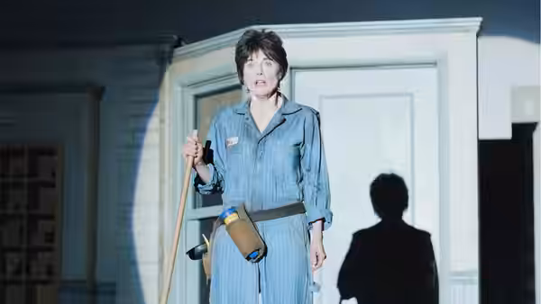 Sybil (Susan Blommaert) holds mop in sunlit room with shadow