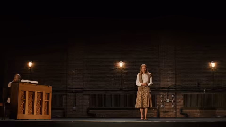 Mona (Julianne Moore) stands onstage near man at wooden podium