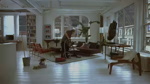 A man vacuums the rug in a bright spacious apartment with bookshelves