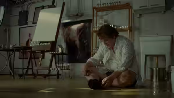 A man sits on the floor of an art studio adjusting his shoe