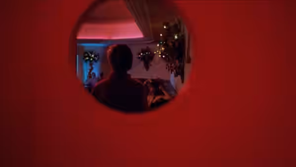 a man viewed from behind through a circular window in a red room