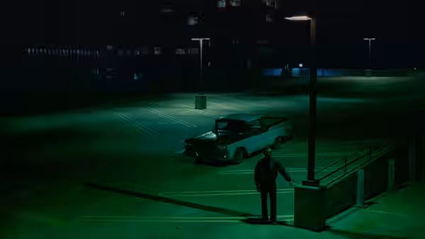 a man standing beside a car in an empty parking lot at night