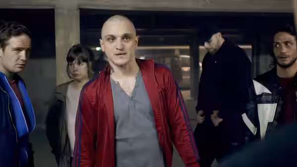 A man in a red jacket stands facing forward with others behind him