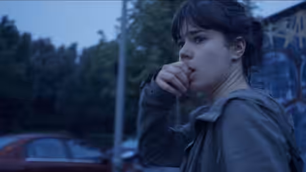 A woman with dark hair in a ponytail stands outdoors at dusk