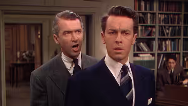 Rupert Cadell (James Stewart) speaks behind Phillip Morgan (Farley Granger) in the apartment library