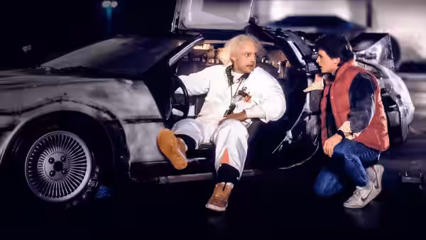 Emmett Brown (Christopher Lloyd) seated in the DeLorean as Marty McFly (Michael J. Fox) kneels beside