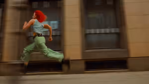 Lola (Franka Potente) running along a city sidewalk past buildings
