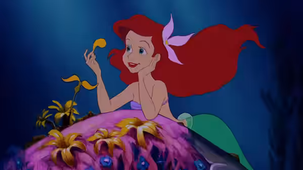 Ariel reclining on a flower-covered rock holding a golden ribbon