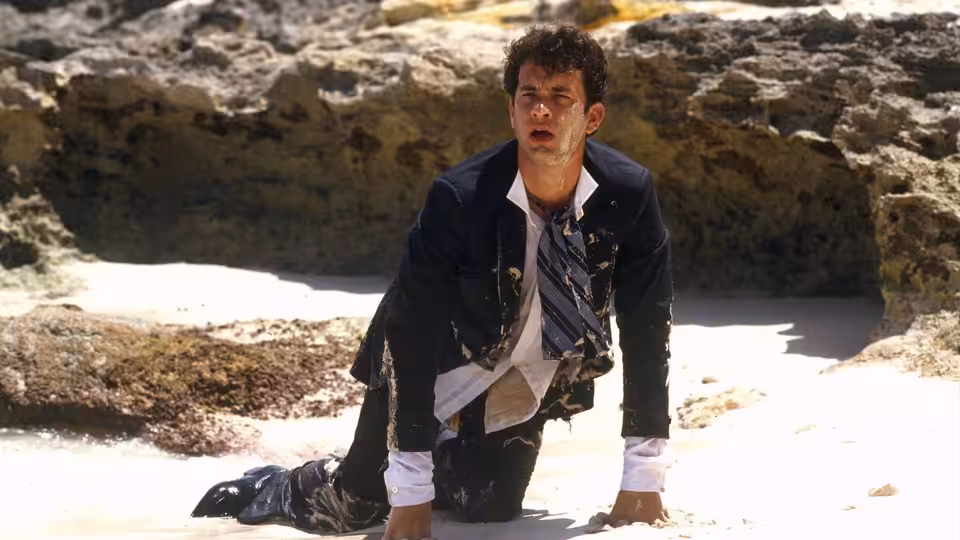 Allen Bauer (Tom Hanks) crawls across a rocky beach in a soaked suit