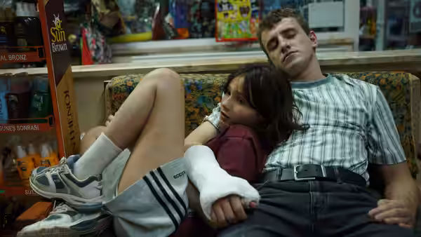 Sophie (Frankie Corio) leans against Calum (Paul Mescal), whose arm is in a sling, inside a shop