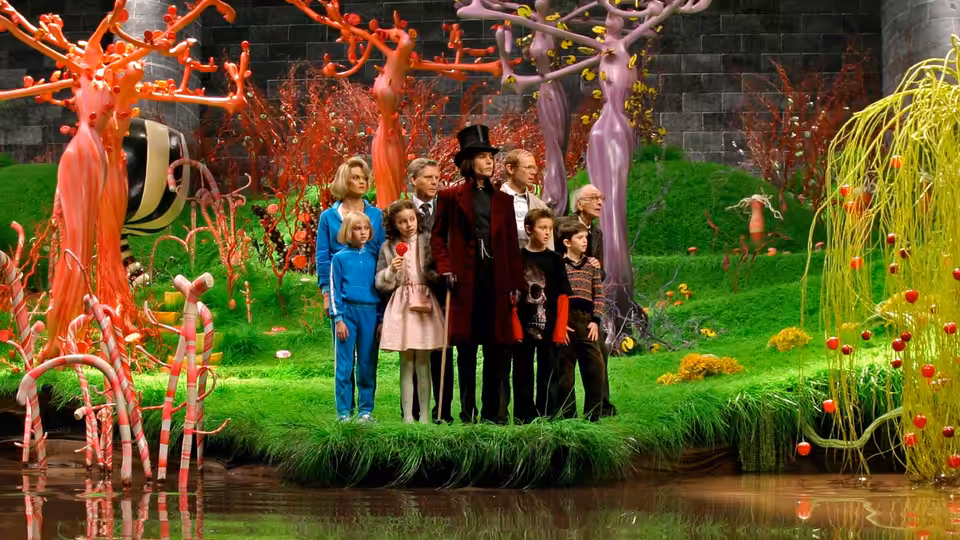Willy Wonka (Johnny Depp) stands with children among colorful trees by a river