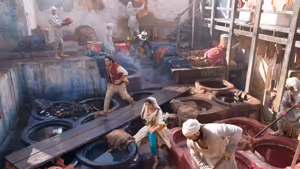 Aladdin (Mena Massoud) leaping across vats in a busy workshop