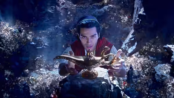 Aladdin (Mena Massoud) holding the golden lamp inside a treasure cave