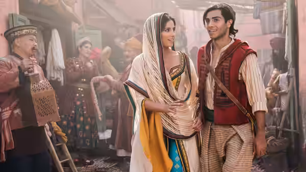 Aladdin (Mena Massoud) and Jasmine (Naomi Scott) walking through a busy marketplace