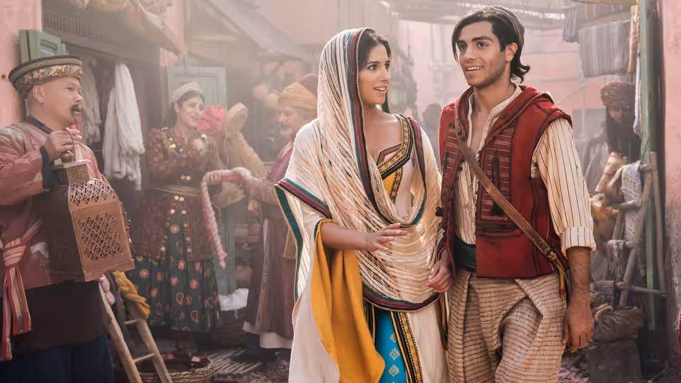 Aladdin (Mena Massoud) and Jasmine (Naomi Scott) walking through a busy marketplace
