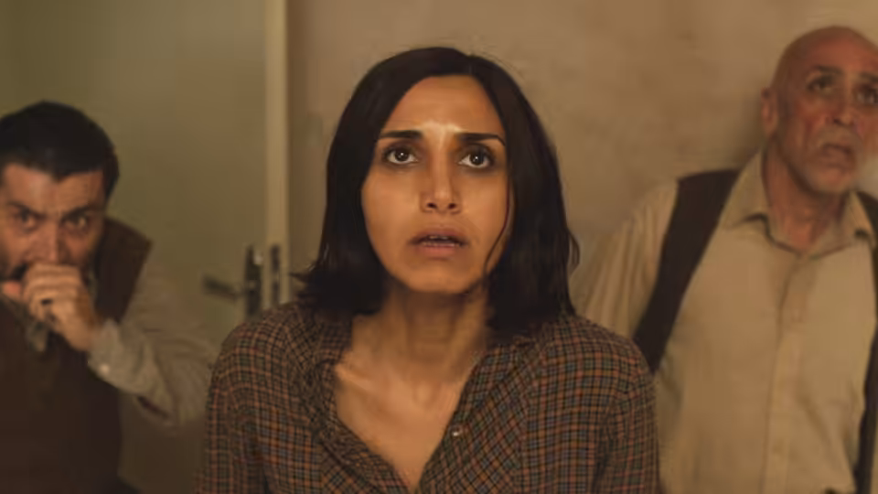 Shideh (Narges Rashidi) and two men look upward inside an apartment