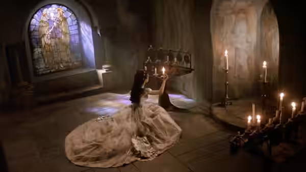 Christine in a white gown kneeling with a candelabra in a stone room