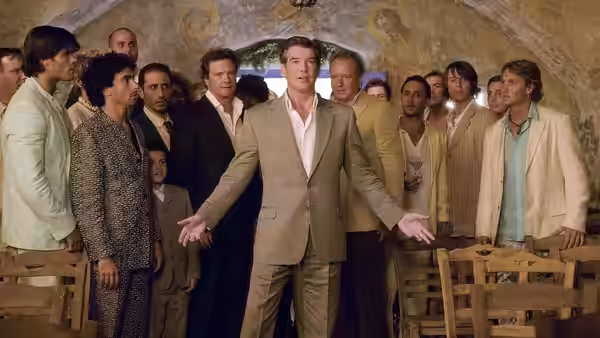 Sam Carmichael (Pierce Brosnan) gestures with arms outstretched among men