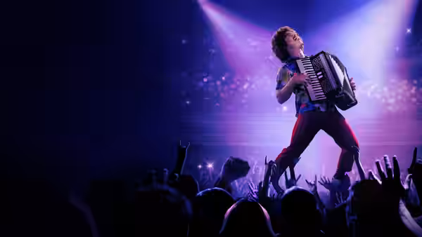Weird Al (Daniel Radcliffe) plays accordion on stage under purple lights before a cheering crowd