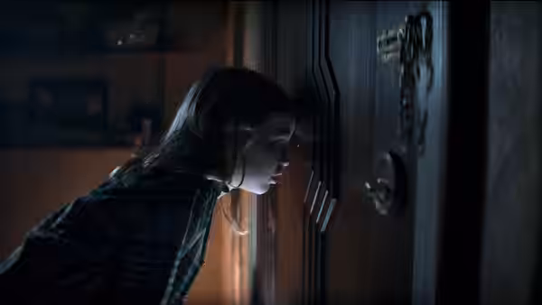 A young girl peering intently through the mail slot of a wooden door
