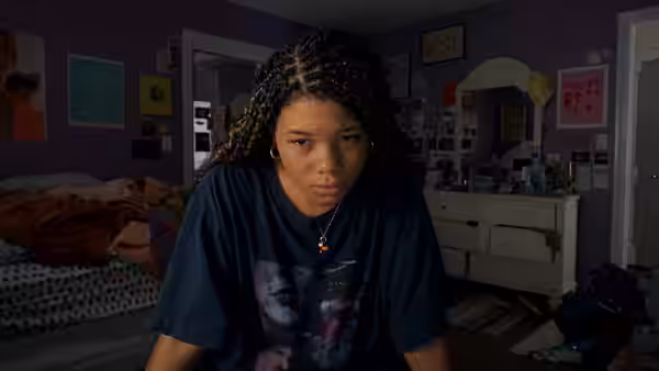 June (Storm Reid) seated in a purple bedroom with a serious expression