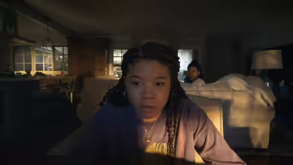 June (Storm Reid) in the foreground of a dark living room at night