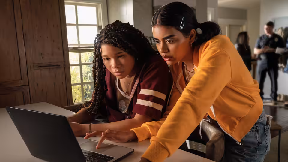 June (Storm Reid) and a friend examining a laptop screen inside a house