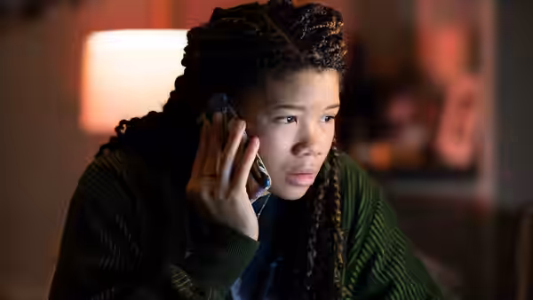 June (Storm Reid) speaking on a cell phone in a green cardigan