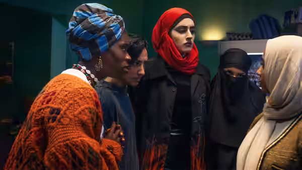 Five women in headscarves huddled closely in a small dimly lit room