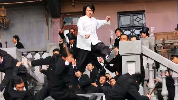 Sing (Stephen Chow) leaps above the stairs as black-suited gang members tumble around him