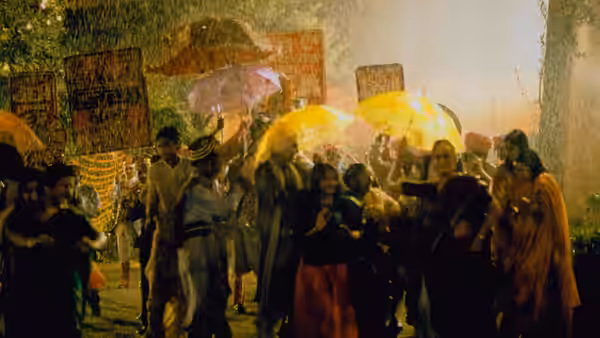 Wedding guests gather beneath yellow umbrellas on a rain-soaked street