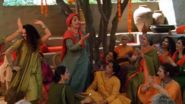 Women gather beneath a tree as one leads a song and dance