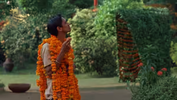 P.K. Dubey (Vijay Raaz) gestures beneath marigold garlands in the garden
