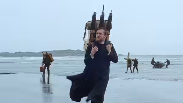 A man carrying a wooden church structure running across a wet beach with others following